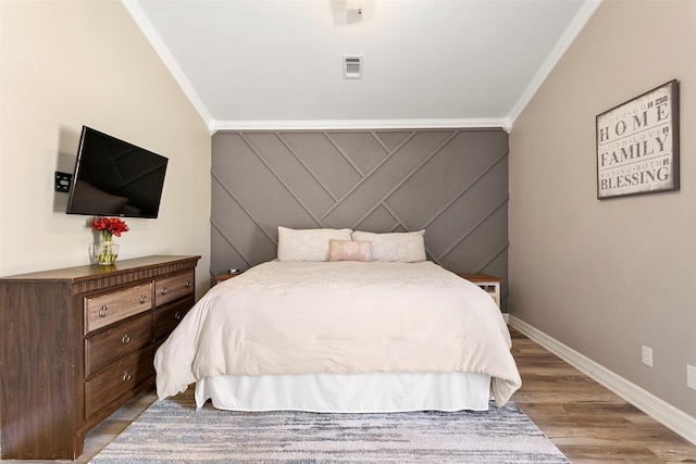 bedroom with baseboards, visible vents, an accent wall, wood finished floors, and crown molding