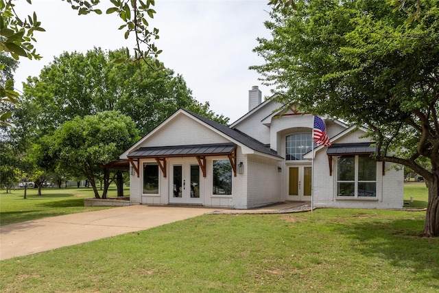 view of front of house featuring a standing seam roof, a chimney, brick siding, and french doors