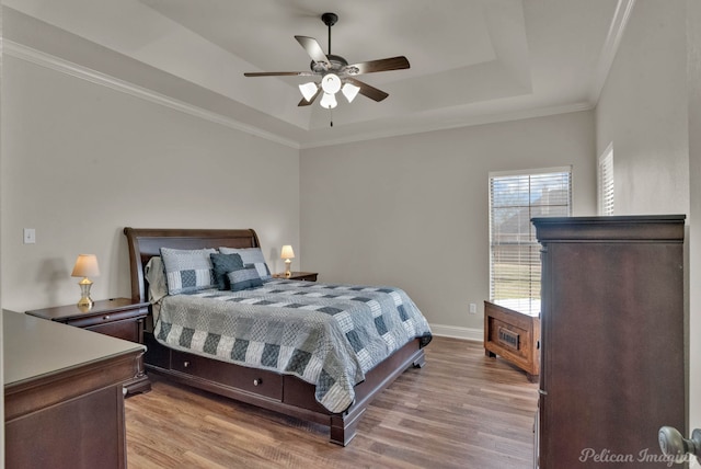 bedroom featuring light wood finished floors, a raised ceiling, ornamental molding, a ceiling fan, and baseboards