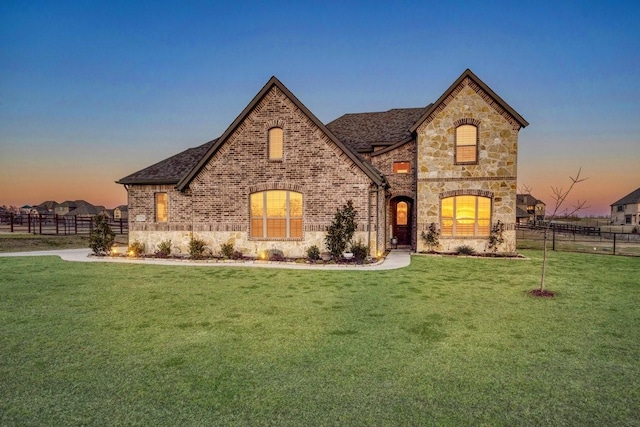 french country home featuring stone siding, brick siding, a front yard, and fence