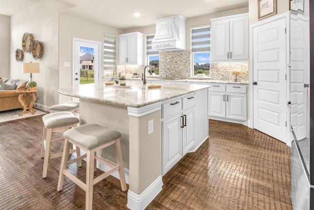 kitchen featuring light stone counters, backsplash, custom exhaust hood, and white cabinetry