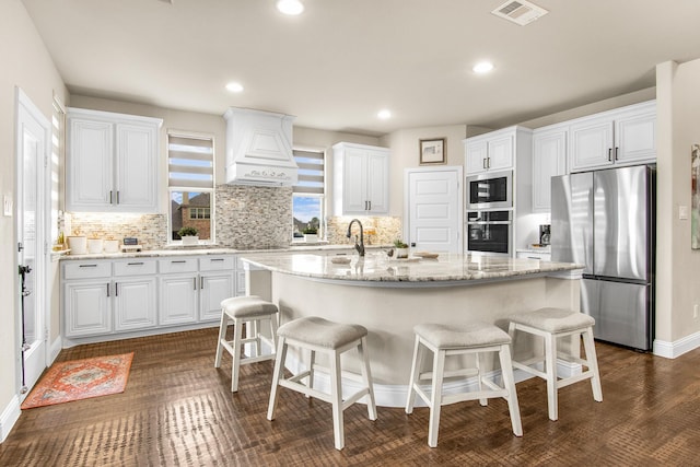 kitchen featuring visible vents, an island with sink, stainless steel appliances, premium range hood, and a kitchen bar