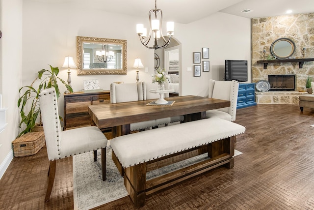 dining space with vaulted ceiling, a stone fireplace, wood finished floors, and an inviting chandelier