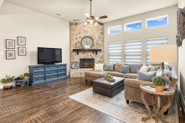 living room featuring visible vents, a towering ceiling, dark wood-style floors, ceiling fan, and a stone fireplace