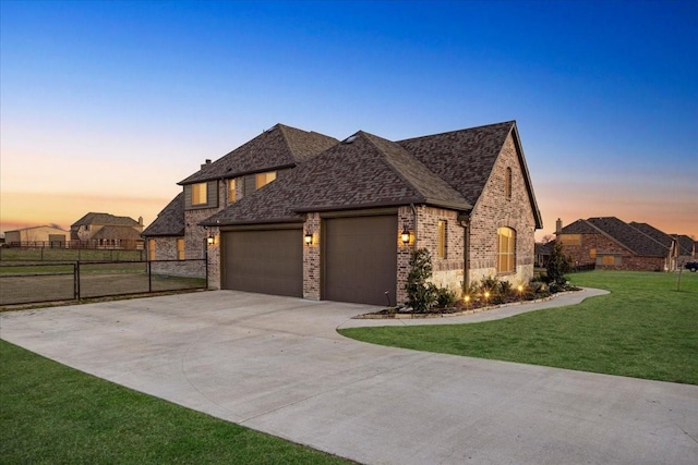 french provincial home featuring a garage, concrete driveway, fence, a yard, and brick siding