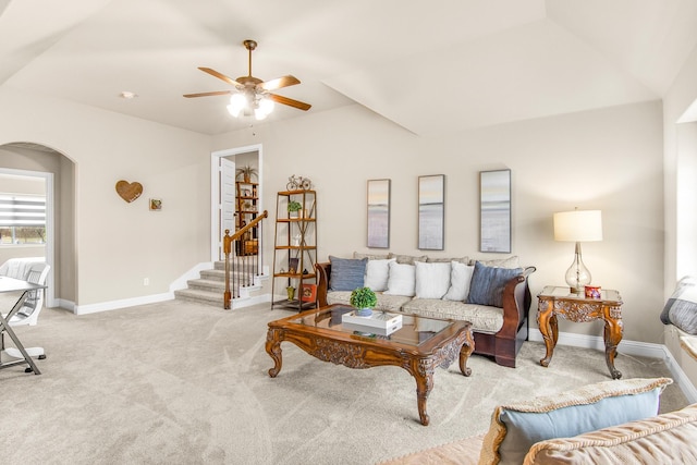 carpeted living room with stairway, baseboards, arched walkways, and a ceiling fan