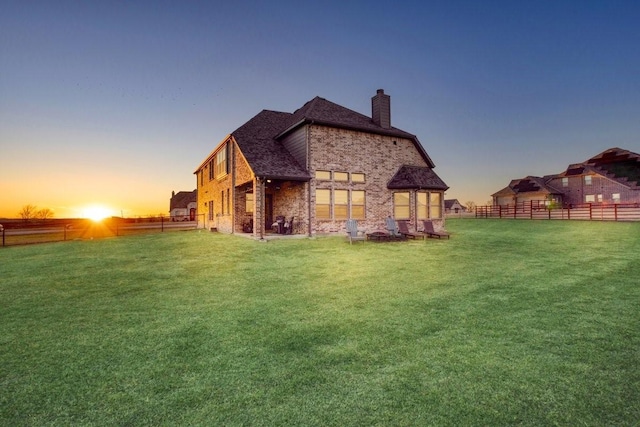 rear view of property with a chimney, fence, a lawn, and brick siding