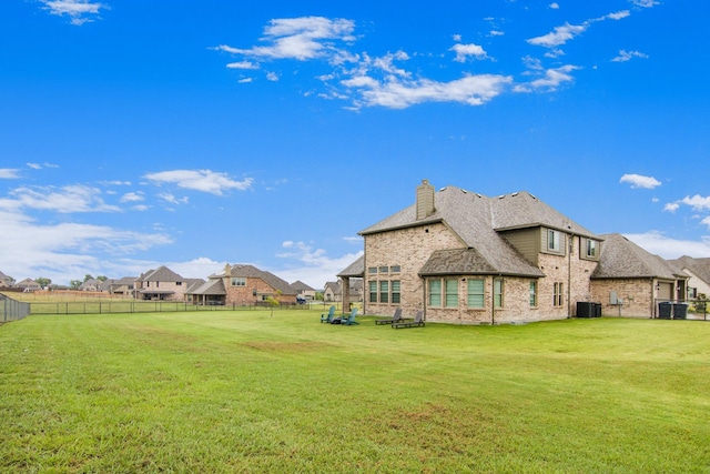 back of property with a fenced backyard, a lawn, a chimney, and central AC unit