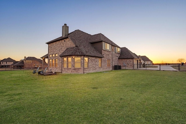 rear view of property featuring brick siding, a chimney, fence, and a yard