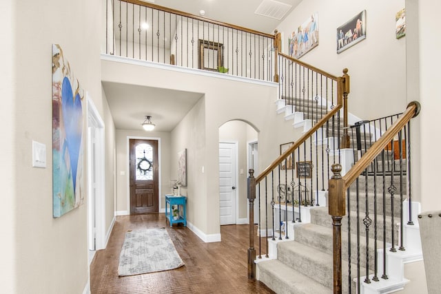 foyer with arched walkways, wood finished floors, a towering ceiling, and baseboards