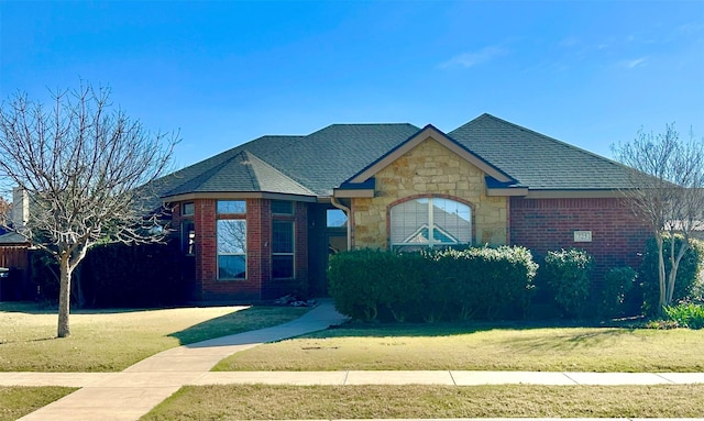 view of front facade featuring a shingled roof, a front yard, stone siding, and brick siding