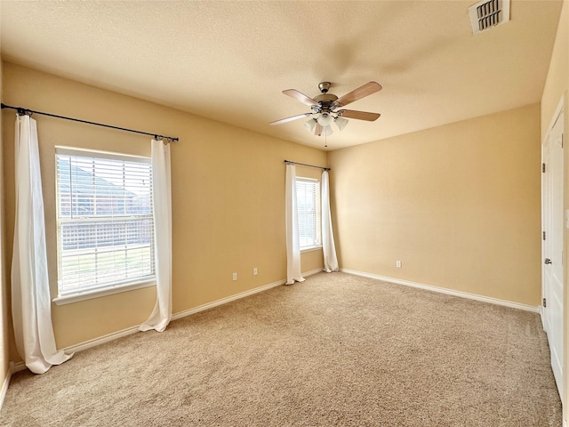 spare room with ceiling fan, a textured ceiling, carpet flooring, visible vents, and baseboards