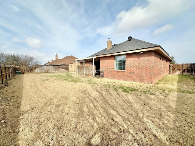 rear view of house with a yard, brick siding, a chimney, and a fenced backyard