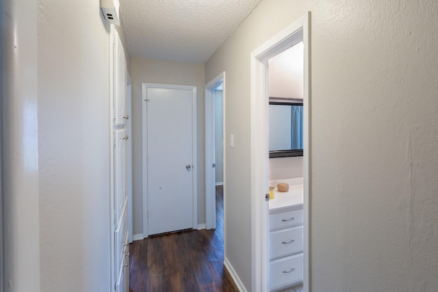 hall featuring a textured ceiling, dark wood-type flooring, and baseboards