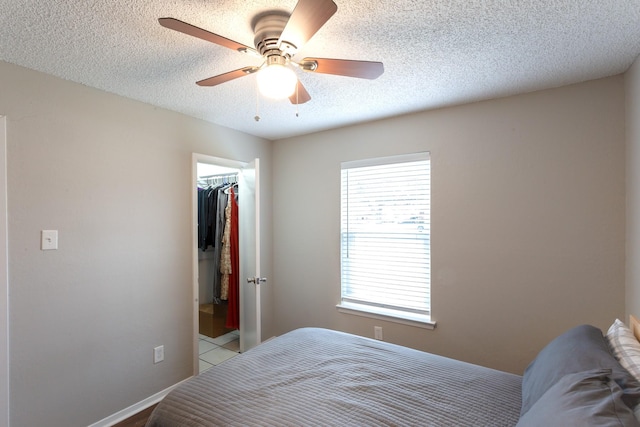 bedroom with a textured ceiling, a ceiling fan, baseboards, a spacious closet, and a closet