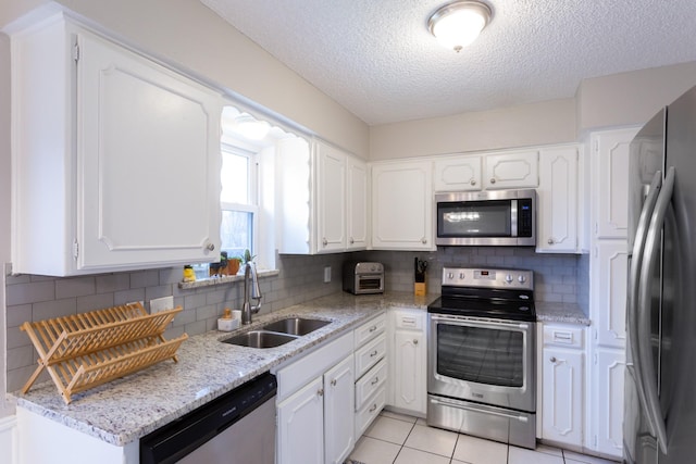 kitchen featuring light tile patterned floors, tasteful backsplash, appliances with stainless steel finishes, white cabinetry, and a sink