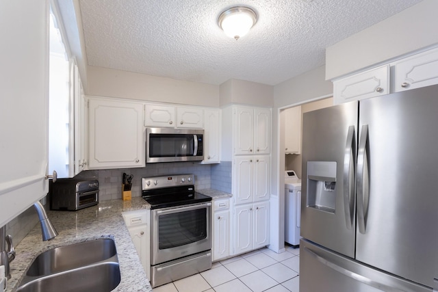 kitchen featuring white cabinets, decorative backsplash, appliances with stainless steel finishes, washer / clothes dryer, and a sink