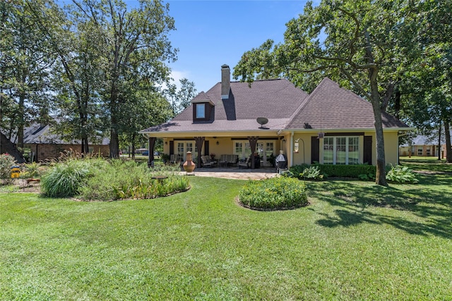 back of property with a patio, a shingled roof, a yard, stucco siding, and a chimney