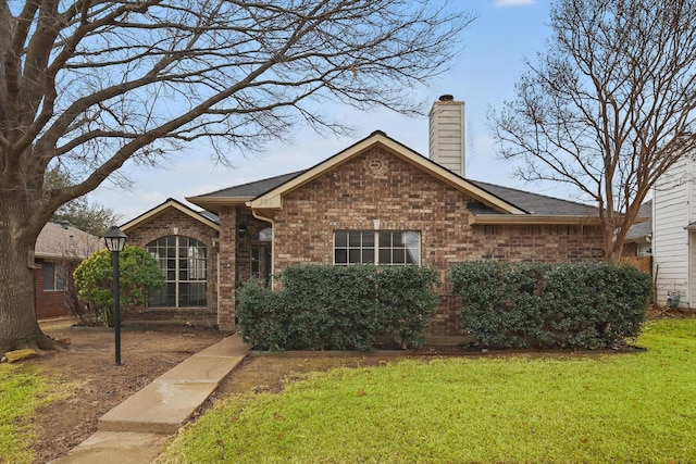 ranch-style house with brick siding, a chimney, and a front yard