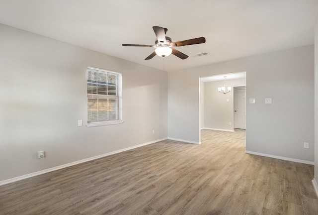 spare room with ceiling fan with notable chandelier, wood finished floors, visible vents, and baseboards