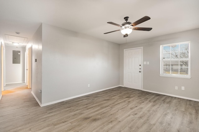 empty room with attic access, light wood-type flooring, ceiling fan, and baseboards