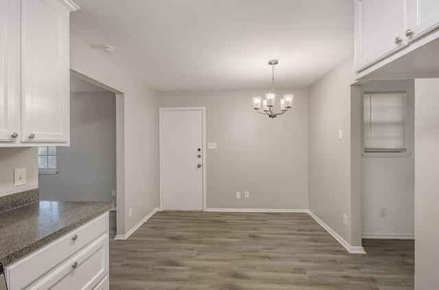 unfurnished dining area with baseboards, wood finished floors, and an inviting chandelier