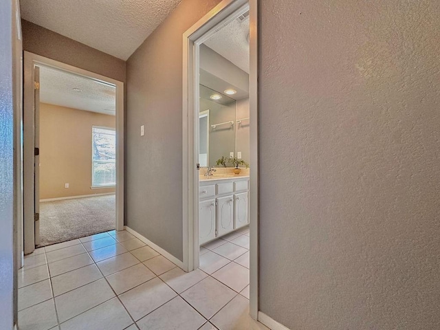 corridor with light tile patterned floors, baseboards, a textured wall, a textured ceiling, and a sink