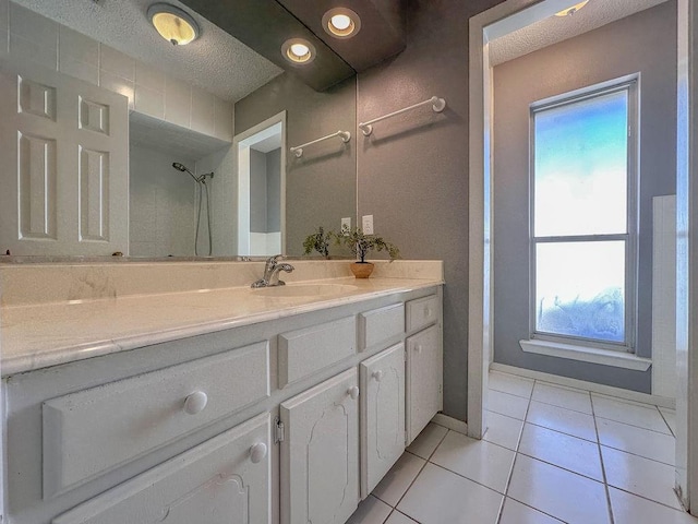 full bathroom featuring a textured ceiling, vanity, baseboards, tile patterned floors, and walk in shower