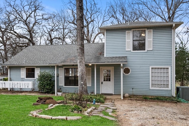 traditional-style house with cooling unit, roof with shingles, and a front yard