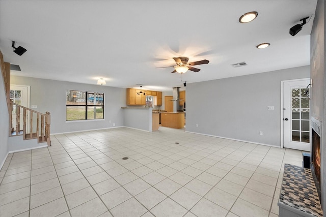 unfurnished living room featuring light tile patterned floors, visible vents, stairway, ceiling fan, and baseboards