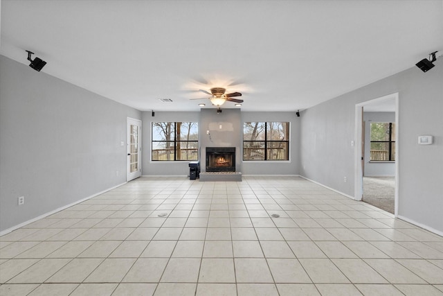 unfurnished living room with a warm lit fireplace, ceiling fan, light tile patterned floors, visible vents, and baseboards