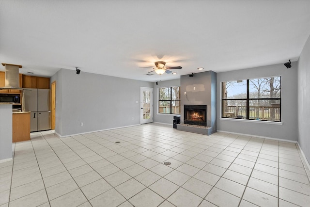 unfurnished living room featuring a ceiling fan, a warm lit fireplace, baseboards, and light tile patterned floors