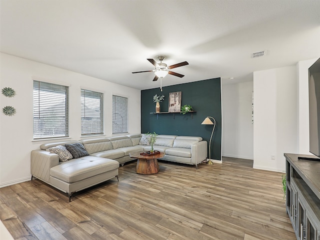 living area with baseboards, a ceiling fan, visible vents, and light wood-style floors