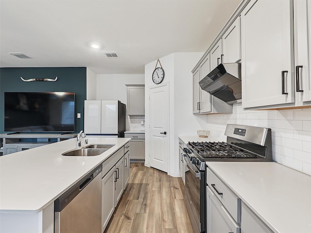 kitchen with light wood-style flooring, under cabinet range hood, a sink, visible vents, and appliances with stainless steel finishes