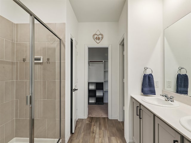 full bathroom featuring a walk in closet, a sink, a shower stall, and wood finished floors