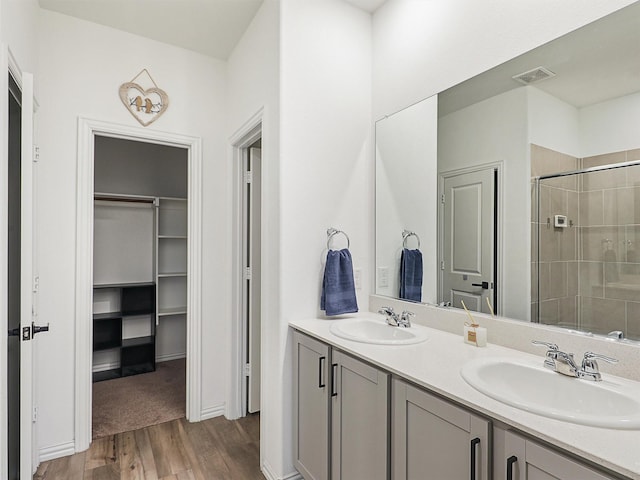 full bath featuring a tile shower, a spacious closet, wood finished floors, and a sink