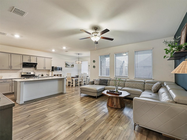 living area featuring a textured ceiling, light wood finished floors, visible vents, and a ceiling fan