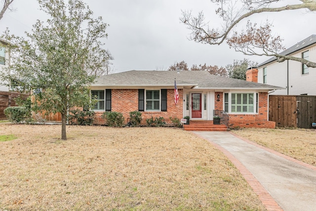 ranch-style home featuring brick siding, a front lawn, a chimney, and fence