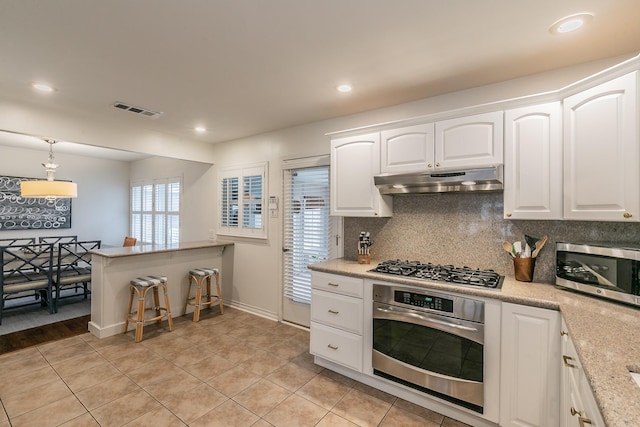 kitchen with under cabinet range hood, visible vents, white cabinets, appliances with stainless steel finishes, and backsplash