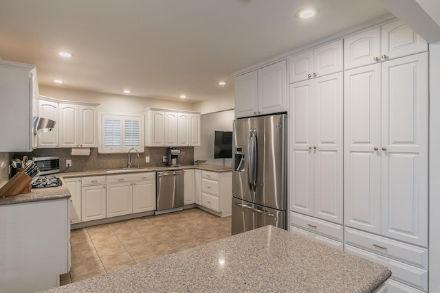 kitchen featuring tasteful backsplash, appliances with stainless steel finishes, light stone counters, a sink, and light tile patterned flooring