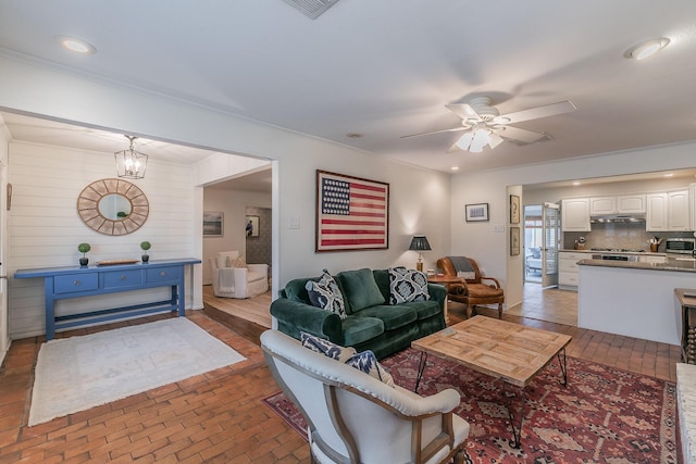 living area featuring ceiling fan with notable chandelier, brick floor, and recessed lighting