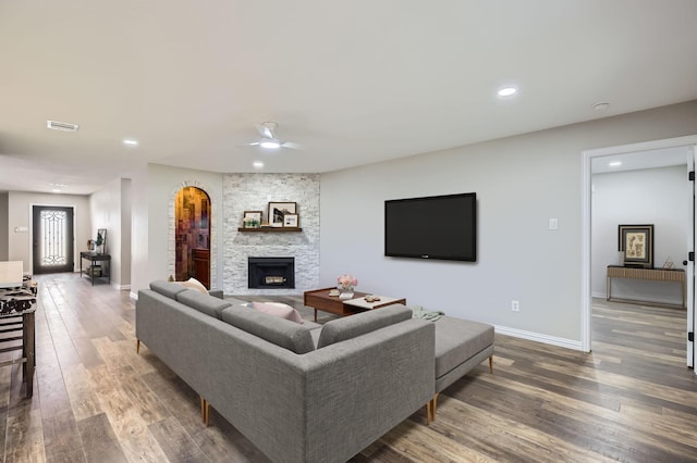 living area featuring visible vents, arched walkways, wood finished floors, and a stone fireplace