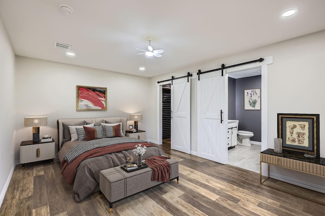 bedroom featuring baseboards, a barn door, visible vents, and wood finished floors