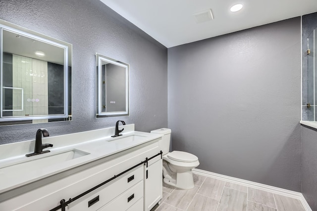 full bath with a textured wall, a sink, toilet, and double vanity