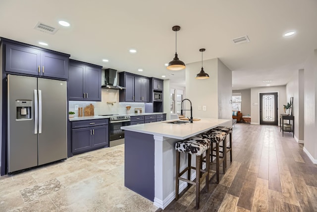 kitchen with a sink, visible vents, a kitchen breakfast bar, appliances with stainless steel finishes, and wall chimney range hood