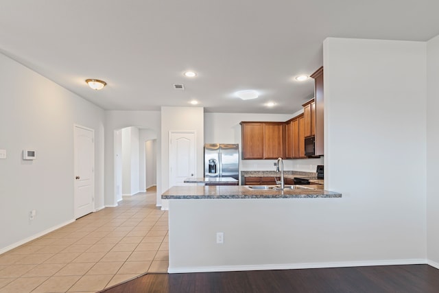 kitchen with arched walkways, a peninsula, a sink, dark stone counters, and black appliances