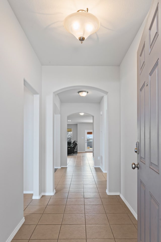 corridor featuring arched walkways, baseboards, and light tile patterned floors