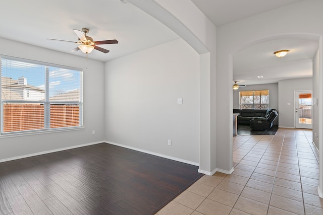 unfurnished room with light wood-style floors, baseboards, arched walkways, and a ceiling fan