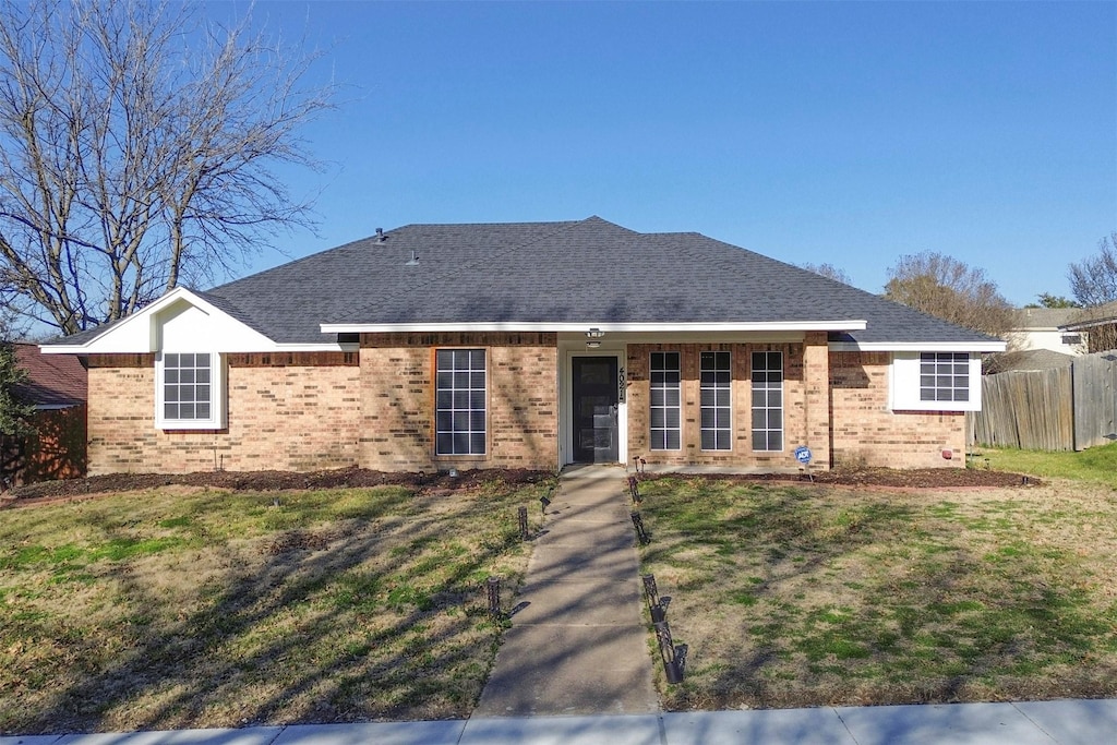 ranch-style home with a front yard, brick siding, fence, and roof with shingles