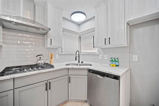 kitchen featuring light stone counters, stainless steel appliances, a sink, wall chimney range hood, and decorative backsplash